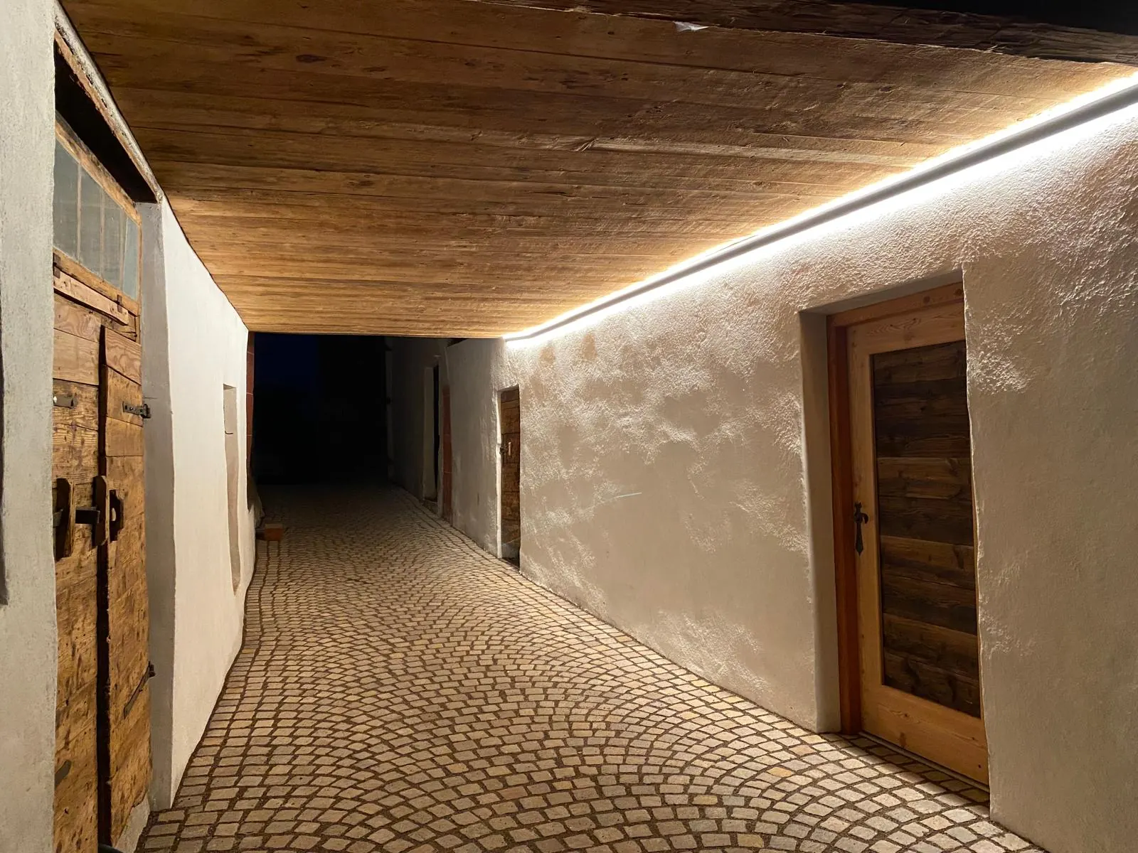 Gepflasterter Durchgang mit durchlaufender LED-Lichtlinie unter der Holzdecke, Schloss Payersberg.