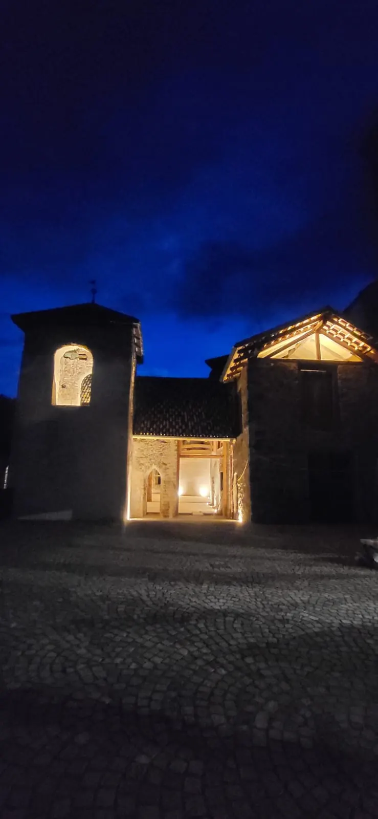 Schloss Payersberg bei Nacht: beleuchteter Giebel, Turm und der erhellte Durchgang über dem gepflasterten Hof.