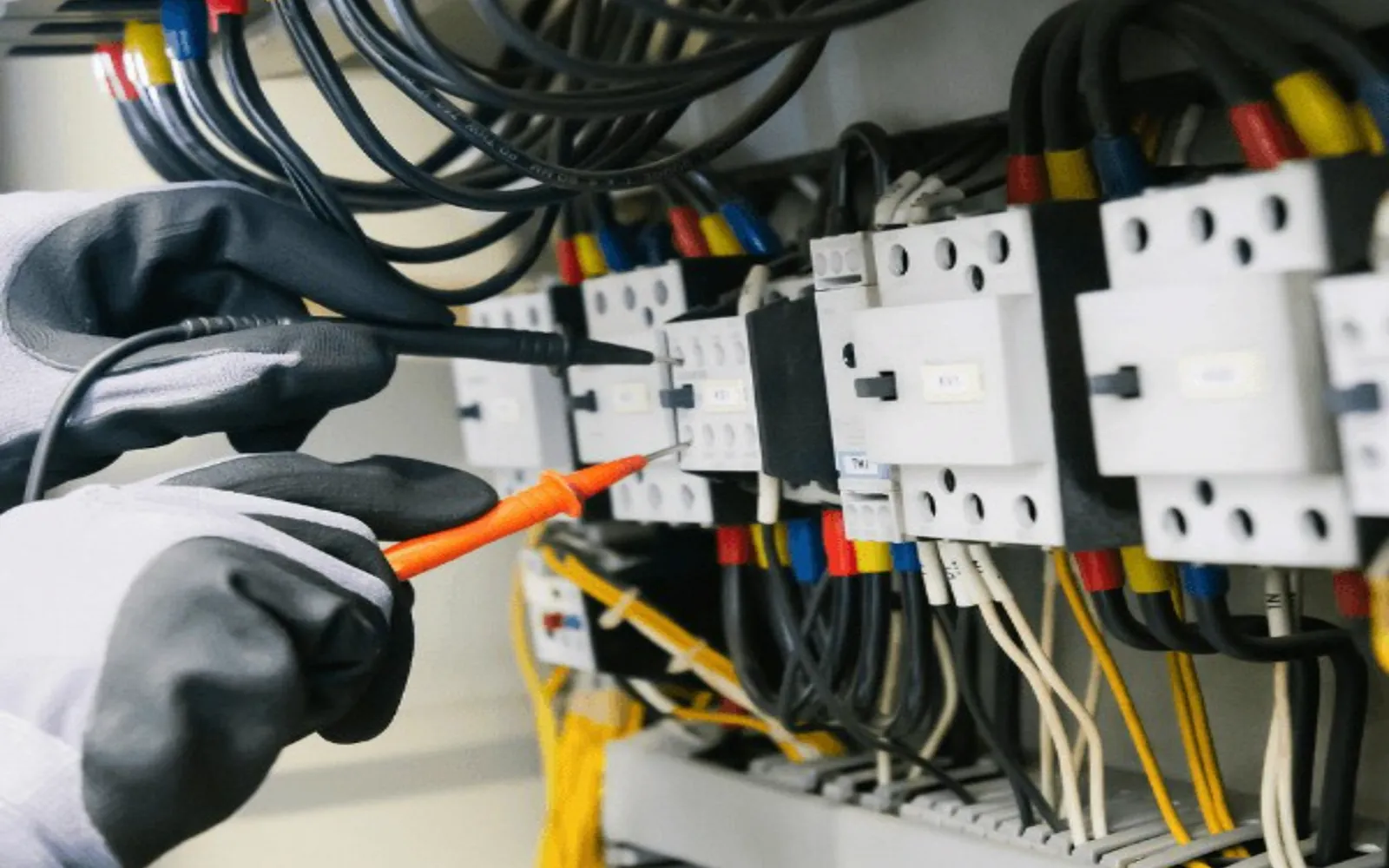 Hände mit Schutzhandschuhen arbeiten an einer Schützreihe im Schaltschrank.